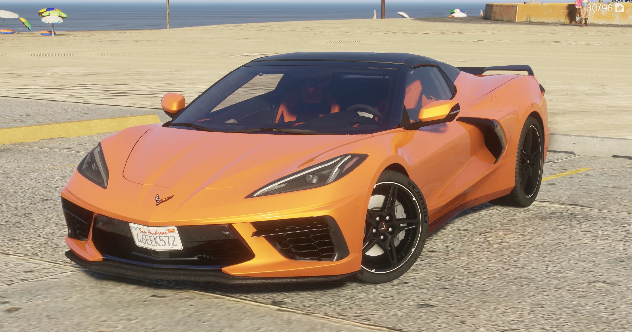 Vista frontal en tres cuartos del Corvette C8 descapotable naranja con el techo duro negro cerrado, aparcado en el paseo de la playa