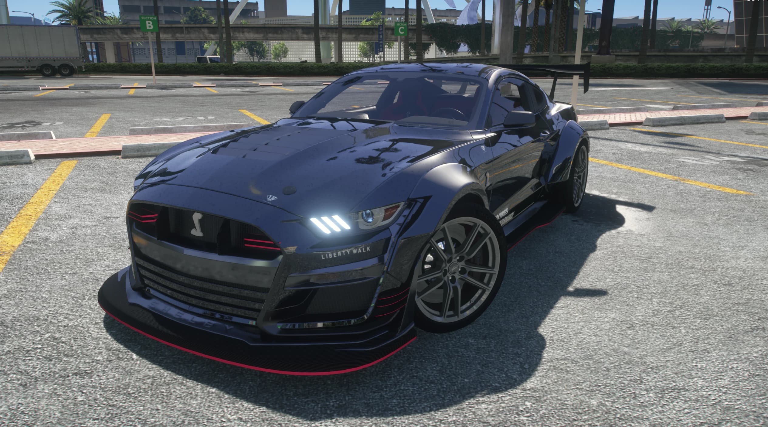 Vista frontal en tres cuartos del GT500 azul oscuro con las letras Liberty Walk en el morro, splitter perfilado en rojo, la cobra en la parrilla y un alerón GT alto