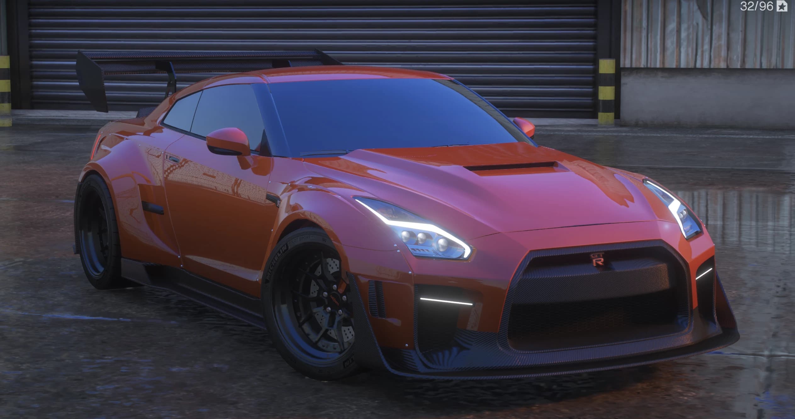 Vista frontal en tres cuartos del Nissan GT-R widebody naranja con canards de carbono, capó ventilado y un gran alerón de carbono ante una persiana de garaje