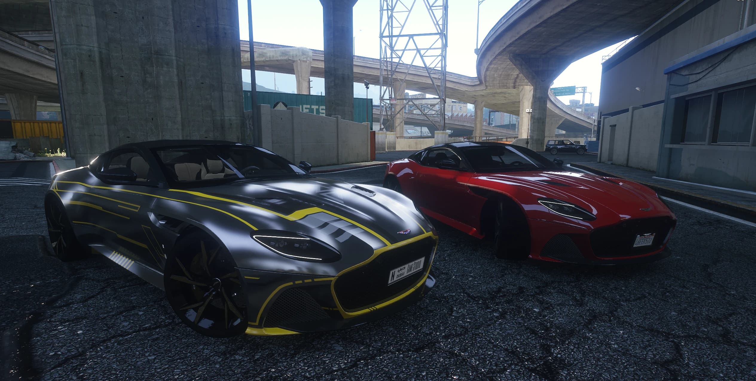 Los dos add-ons del DBS Superleggera aparcados juntos bajo una autopista: uno gris con una decoración amarilla estilo tron y otro rojo liso