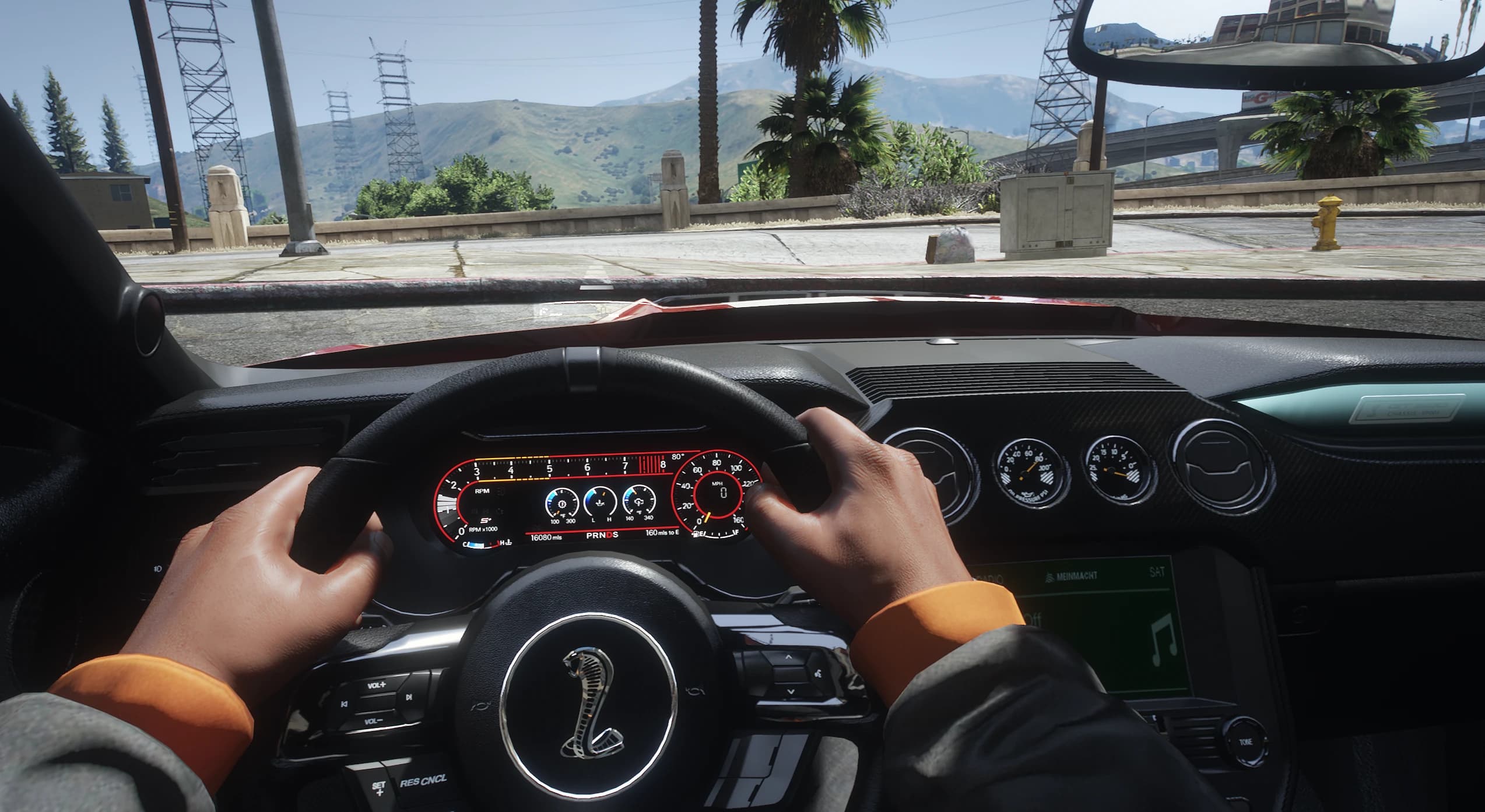 Vista en primera persona al volante con el cuadro digital, los relojes auxiliares del salpicadero y la cobra en el volante