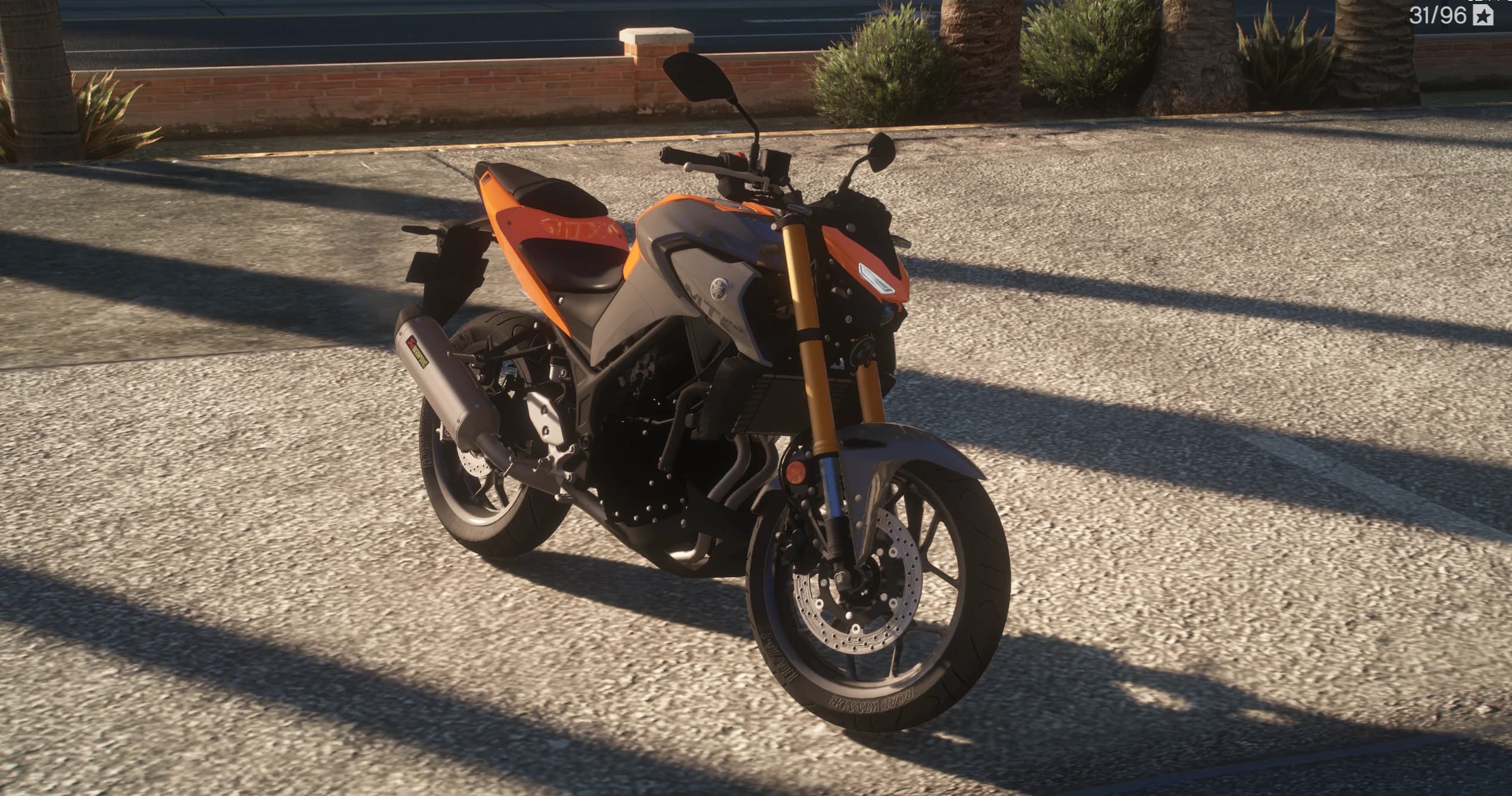Vista frontal en tres cuartos de la Yamaha MT-03 naranja y gris con horquilla invertida dorada, doble disco delantero y silencioso Akrapovic, aparcada junto a un muro de ladrillo