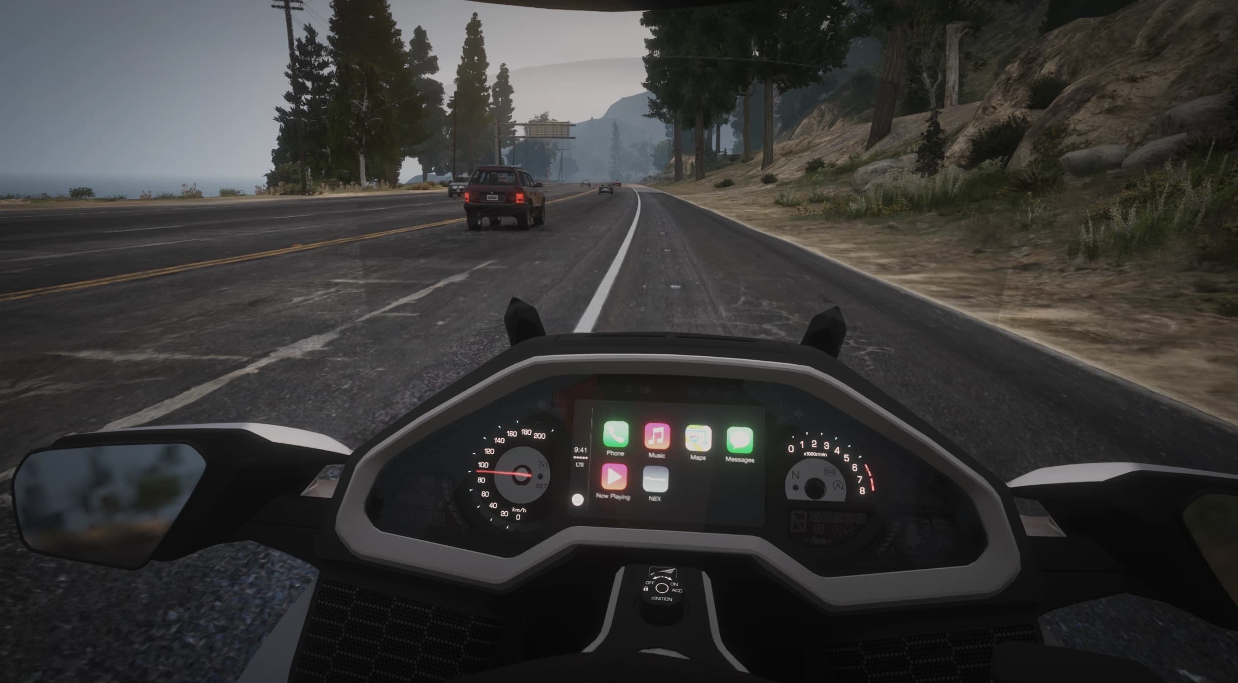 Vista en primera persona por una carretera costera con el salpicadero completo de la Goldwing, velocímetro y cuentavueltas analógicos y la pantalla central con las apps de teléfono, música y mapas