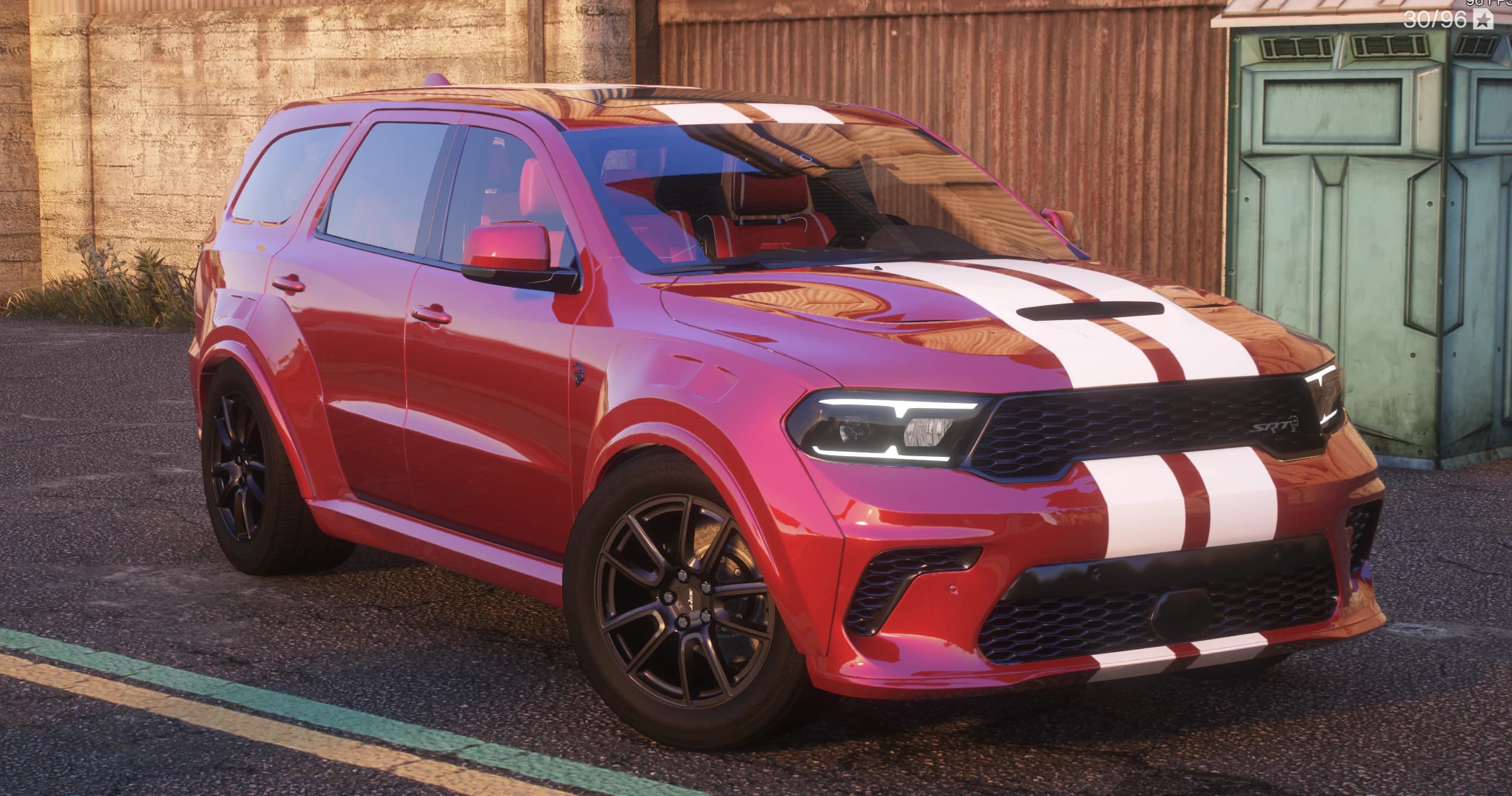 Todoterreno Dodge Durango Widebody 2021 en rojo con dos franjas blancas de competición sobre el techo y el capó, vista frontal en tres cuartos junto a un contenedor verde, con el emblema SRT de la parrilla, los faros LED finos y llantas negras multirradio