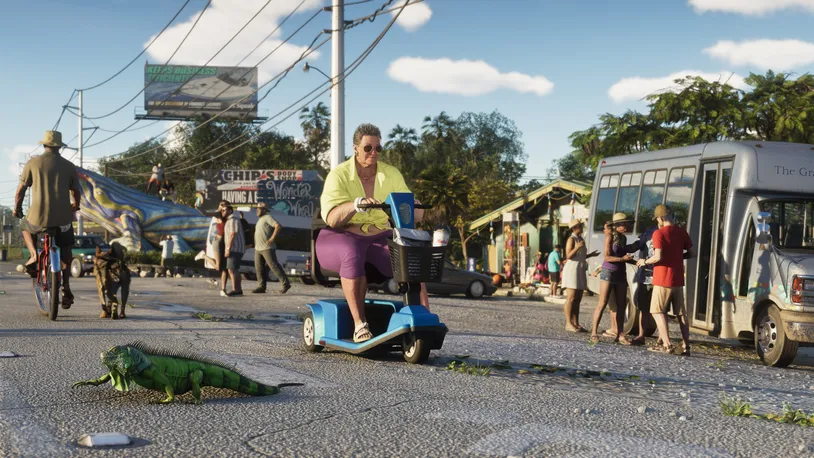 Una calle concurrida de Vice City con peatones, ciclistas, un autobús urbano y una mujer en un scooter de movilidad, con una iguana cruzando la calzada