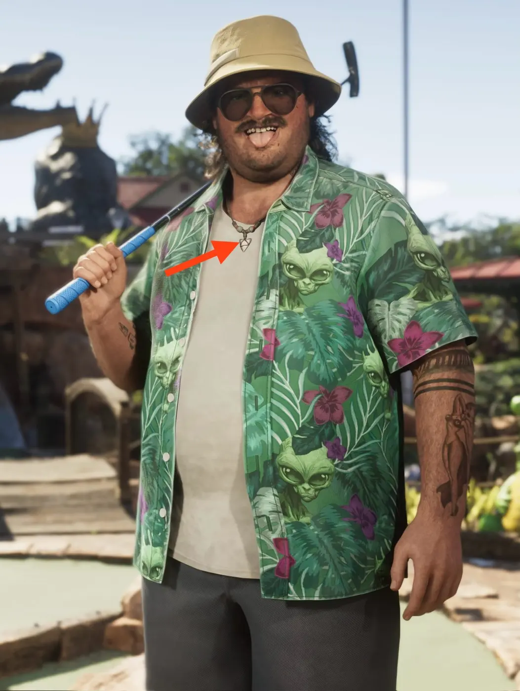 Un personaje corpulento de GTA Online con una camisa tropical verde llena de caras de alienígenas, gorro de pescador y gafas de sol, sosteniendo un palo de golf, con una flecha roja señalando un colgante de reloj de arena en un collar de cuentas igual al que lleva la pintora Rae.